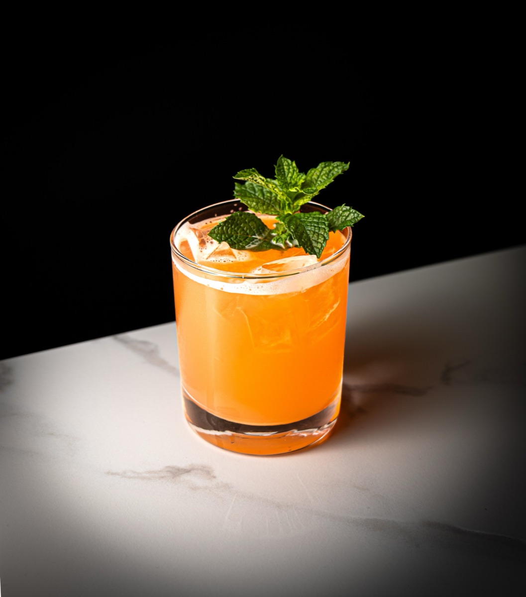 An orange Bravado drink over ice with fresh mint